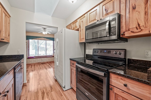 kitchen with appliances with stainless steel finishes, light wood-type flooring, ceiling fan, dark stone counters, and light brown cabinetry