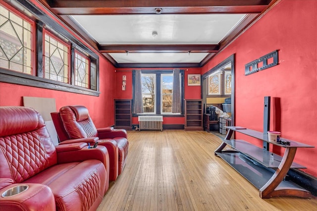 home theater room featuring radiator, hardwood / wood-style floors, crown molding, and beamed ceiling