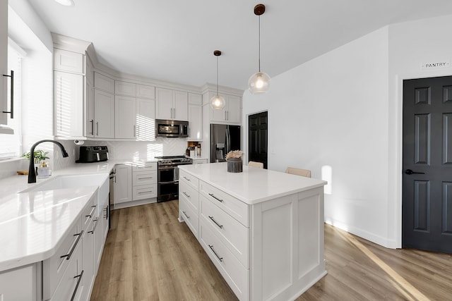 kitchen featuring a center island, sink, decorative light fixtures, white cabinetry, and stainless steel appliances