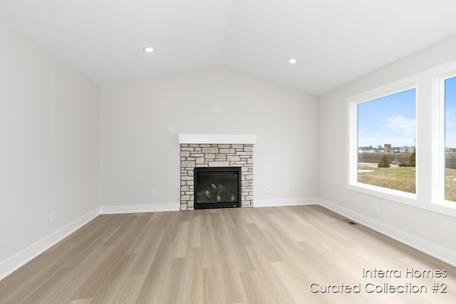 unfurnished living room featuring baseboards, vaulted ceiling, a stone fireplace, light wood-style floors, and recessed lighting