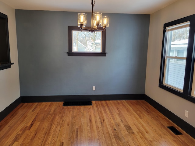 unfurnished room featuring a chandelier and light hardwood / wood-style floors