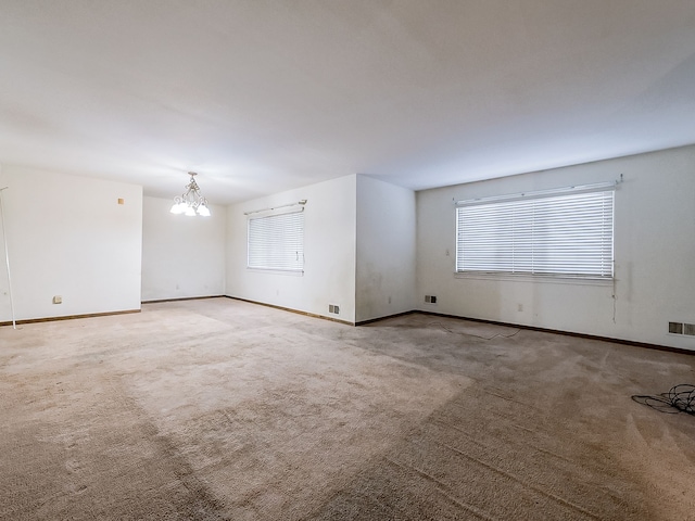 carpeted spare room featuring an inviting chandelier