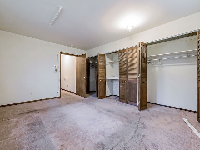 unfurnished bedroom featuring light carpet and two closets