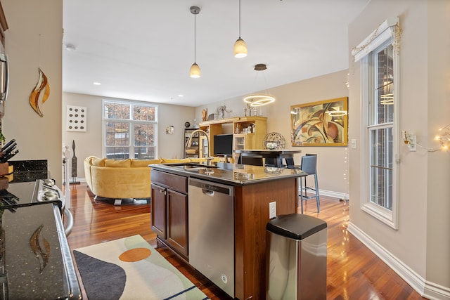 kitchen featuring a kitchen island with sink, dark stone counters, sink, decorative light fixtures, and stainless steel dishwasher