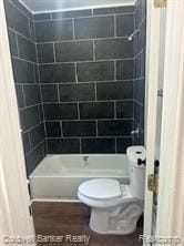 bathroom with hardwood / wood-style floors, tiled shower / bath combo, and toilet