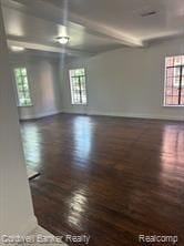 empty room with beamed ceiling, a healthy amount of sunlight, and dark hardwood / wood-style floors