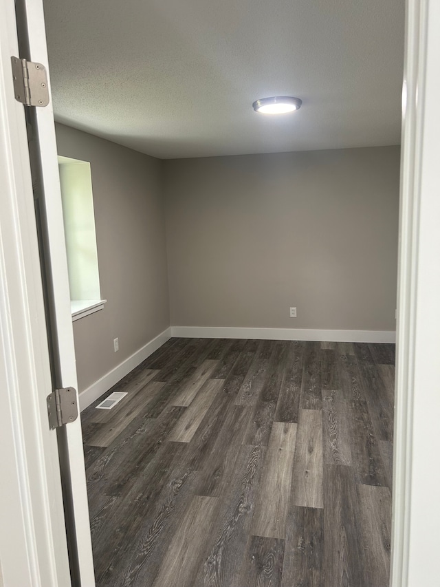 unfurnished room featuring dark wood-type flooring and a textured ceiling