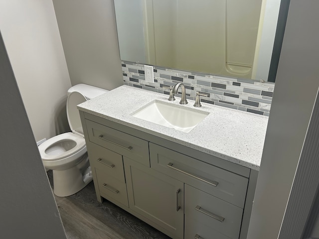 bathroom with hardwood / wood-style floors, backsplash, vanity, and toilet