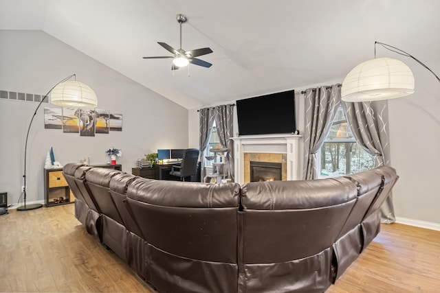 living room featuring vaulted ceiling, ceiling fan, a tiled fireplace, and light hardwood / wood-style floors