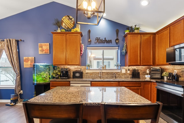 kitchen with lofted ceiling, light stone counters, hanging light fixtures, and sink