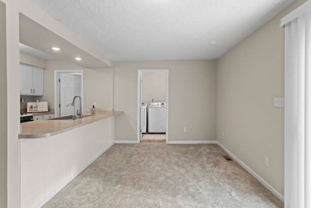 kitchen featuring light colored carpet, washing machine and dryer, sink, a textured ceiling, and white cabinets