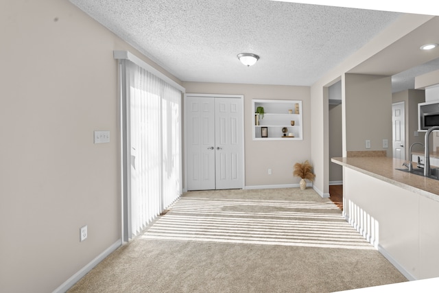 hallway featuring a textured ceiling, carpet flooring, built in features, and sink