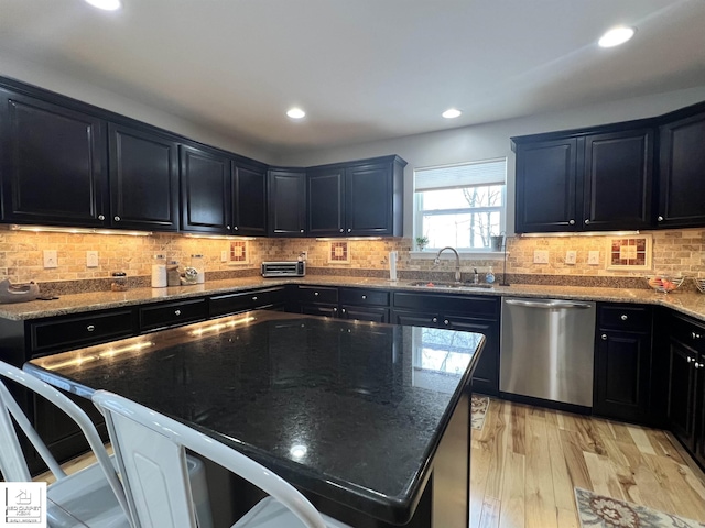 kitchen with sink, dishwasher, light wood-type flooring, dark stone countertops, and a kitchen island