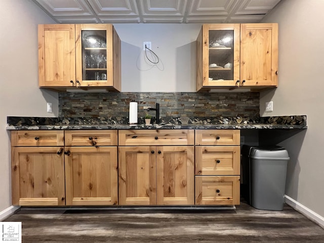 kitchen featuring dark wood-type flooring, light brown cabinetry, dark stone countertops, and tasteful backsplash