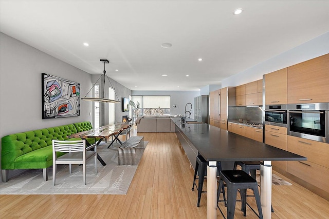 kitchen with sink, appliances with stainless steel finishes, a kitchen breakfast bar, light hardwood / wood-style floors, and decorative light fixtures