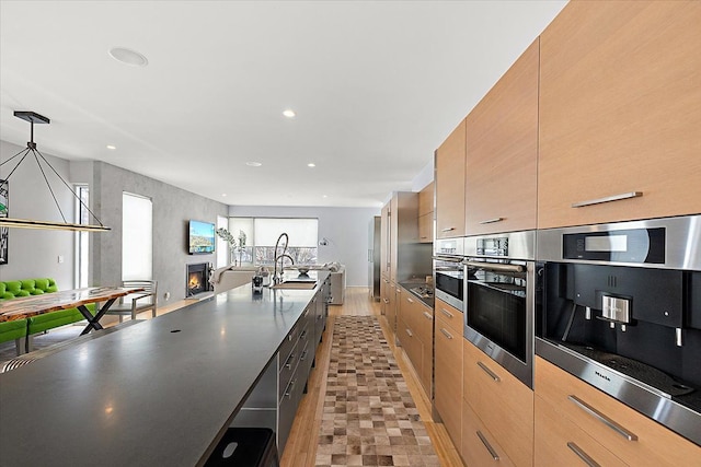 kitchen with hanging light fixtures, sink, light brown cabinets, and oven