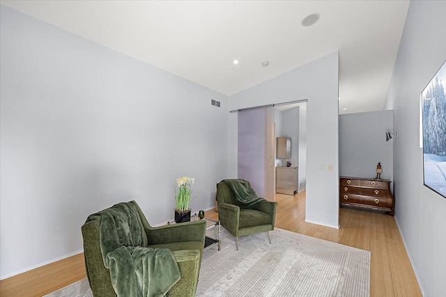 sitting room featuring lofted ceiling, wood-type flooring, and a barn door