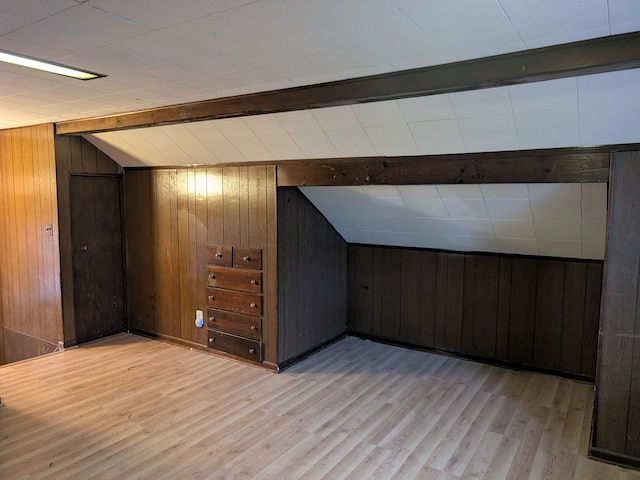 bonus room with light hardwood / wood-style flooring, wood walls, and lofted ceiling with beams