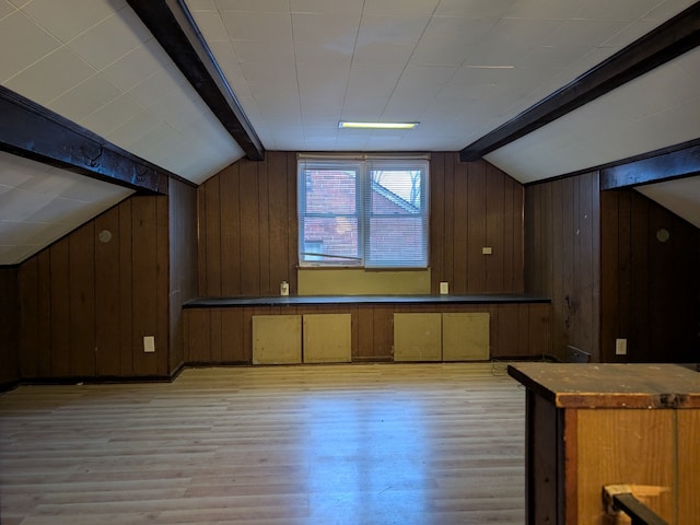 additional living space featuring light wood-type flooring, wood walls, and lofted ceiling with beams