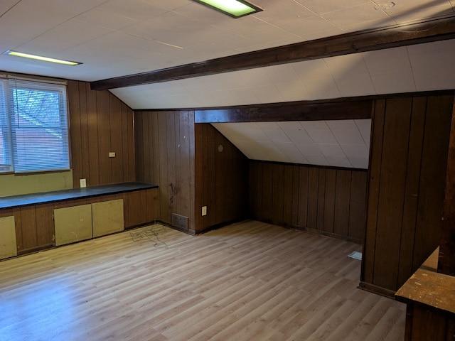 bonus room featuring vaulted ceiling with beams, wooden walls, and light hardwood / wood-style flooring