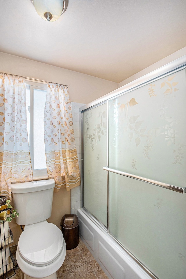 bathroom featuring toilet, tile patterned floors, and combined bath / shower with glass door