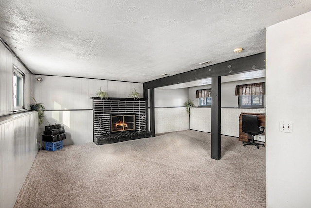 unfurnished living room featuring a tiled fireplace, carpet, a textured ceiling, and visible vents