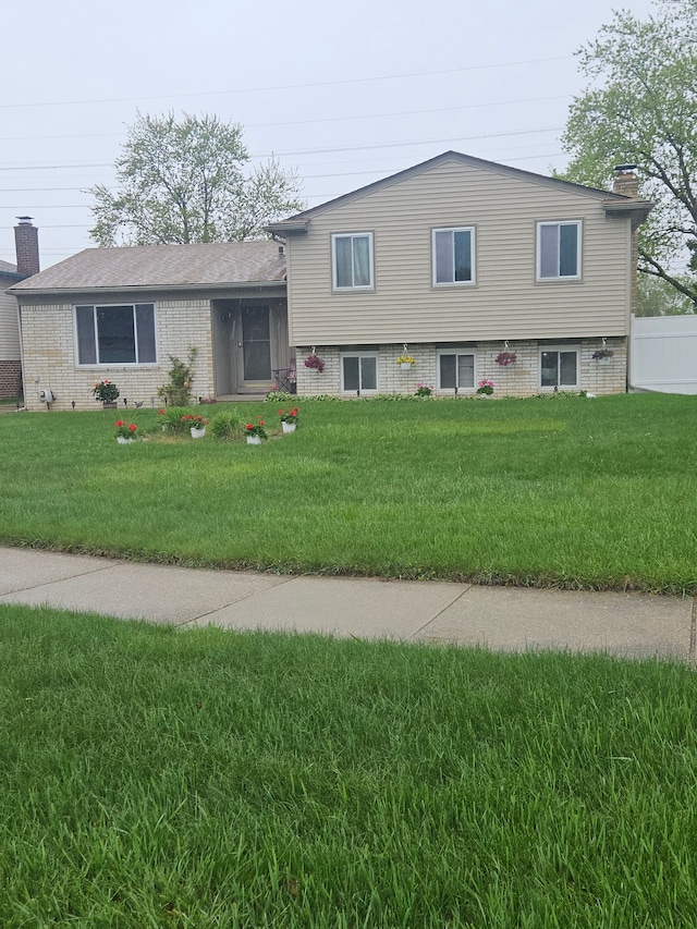 split level home with brick siding, a chimney, and a front lawn