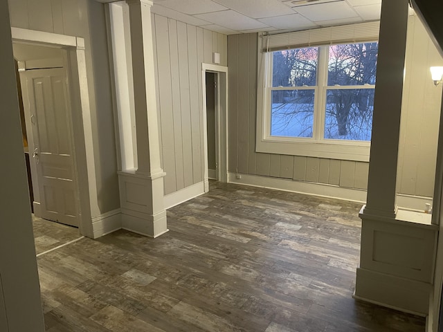 unfurnished room featuring dark wood-type flooring, a drop ceiling, and ornate columns