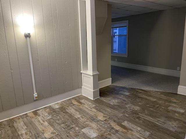 spare room with a paneled ceiling, dark hardwood / wood-style flooring, and wood walls