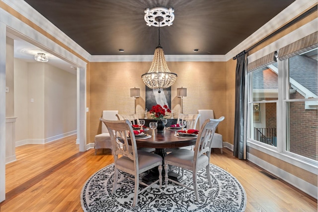 dining area with light hardwood / wood-style floors, ornamental molding, and an inviting chandelier