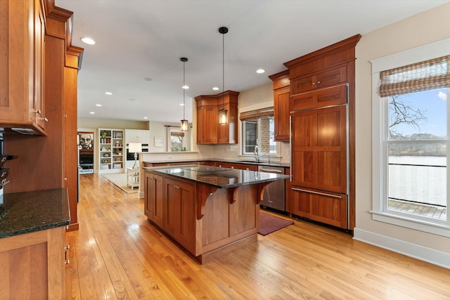 kitchen featuring pendant lighting, dishwasher, a breakfast bar, dark stone counters, and sink