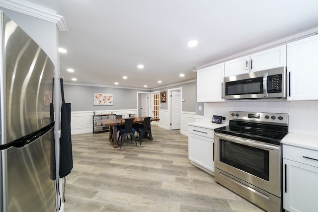 kitchen featuring white cabinetry, ornamental molding, light hardwood / wood-style floors, and appliances with stainless steel finishes