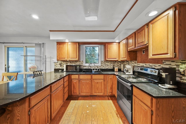 kitchen with kitchen peninsula, stainless steel range with electric stovetop, dark stone counters, sink, and light hardwood / wood-style floors