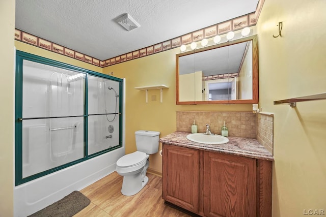 full bathroom with backsplash, bath / shower combo with glass door, vanity, a textured ceiling, and toilet