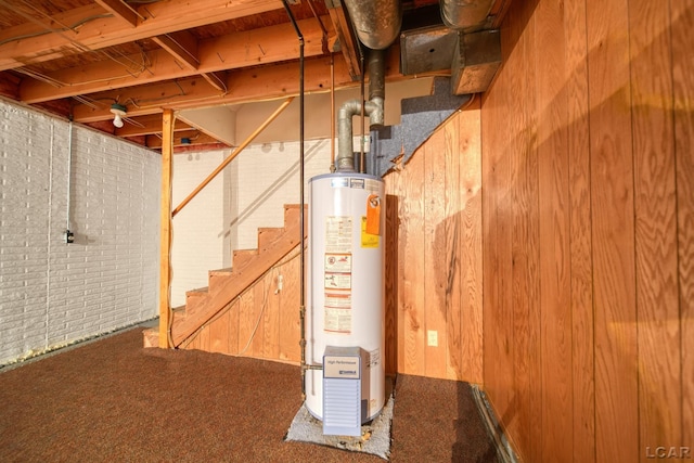 basement featuring carpet, wood walls, gas water heater, and brick wall