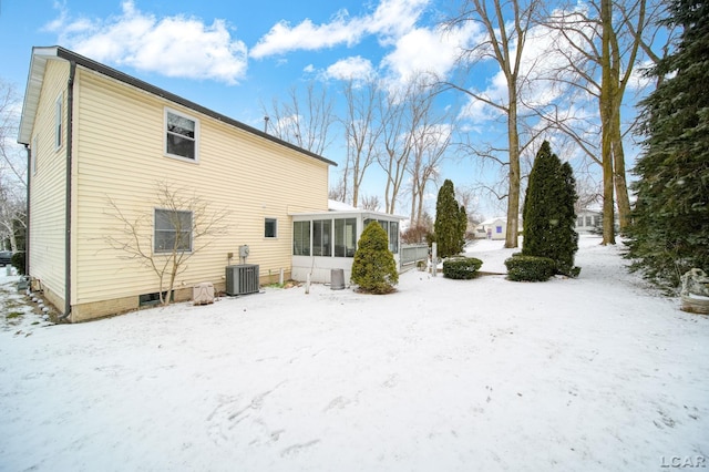 snow covered back of property with central AC unit and a sunroom