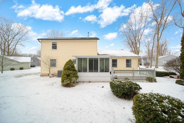 snow covered house with central air condition unit and a sunroom