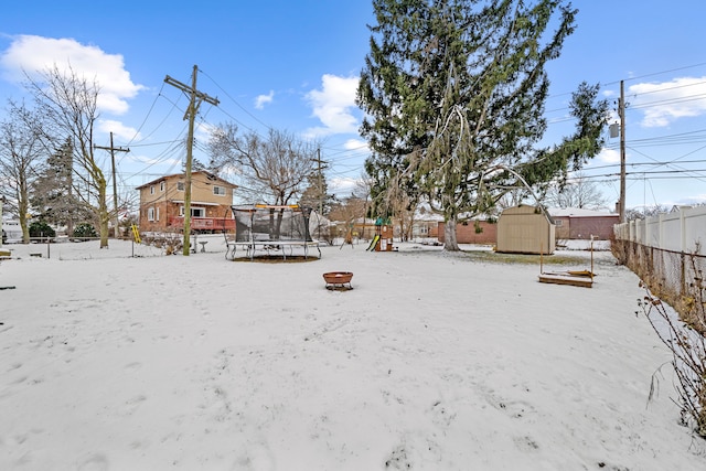 snowy yard featuring a playground, a trampoline, a storage unit, and a fire pit