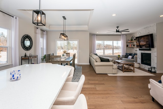 dining area featuring light wood-type flooring, ceiling fan, a fireplace, and a raised ceiling