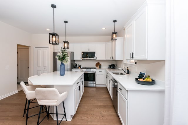 kitchen with white cabinets, appliances with stainless steel finishes, a kitchen island, wood-type flooring, and sink