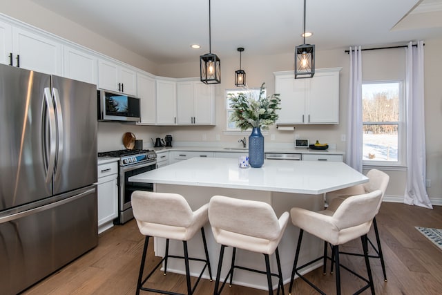 kitchen featuring pendant lighting, a center island, hardwood / wood-style flooring, appliances with stainless steel finishes, and white cabinets