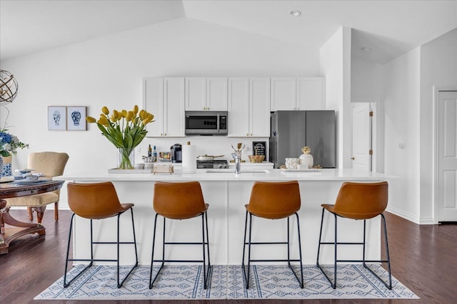 kitchen featuring vaulted ceiling, appliances with stainless steel finishes, white cabinetry, and a kitchen island with sink