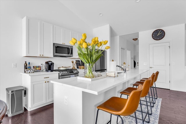 kitchen with white cabinets, dark wood-type flooring, stainless steel appliances, a kitchen island with sink, and a breakfast bar