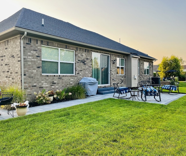 back house at dusk featuring a patio area and a lawn