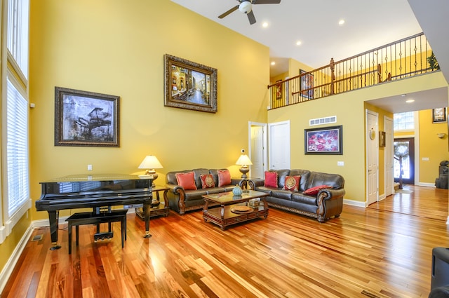 living room with a high ceiling, ceiling fan, and light hardwood / wood-style flooring