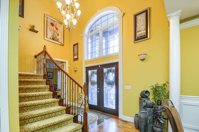 entrance foyer featuring an inviting chandelier, decorative columns, a towering ceiling, french doors, and hardwood / wood-style floors