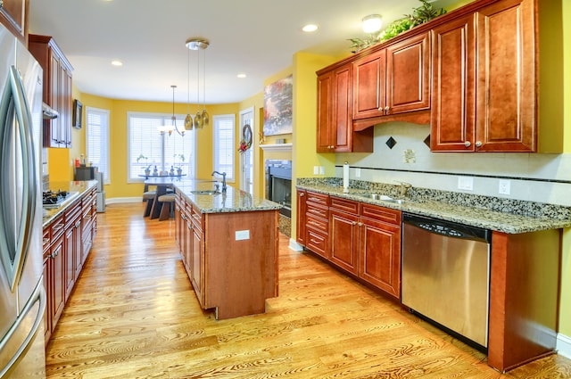 kitchen with a kitchen island with sink, stainless steel appliances, pendant lighting, light stone counters, and an inviting chandelier