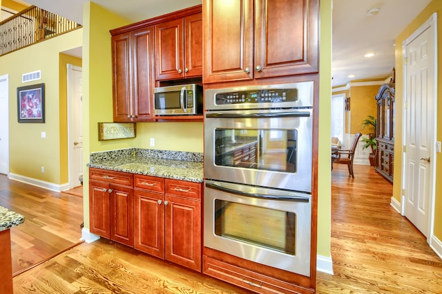 kitchen with appliances with stainless steel finishes, light hardwood / wood-style flooring, ornamental molding, and light stone countertops