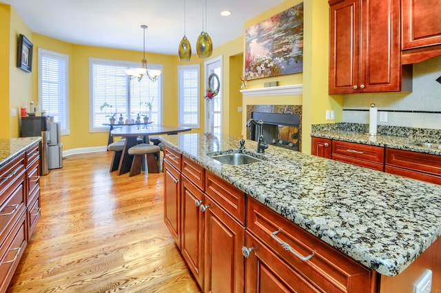 kitchen with sink, an island with sink, decorative light fixtures, and light stone countertops