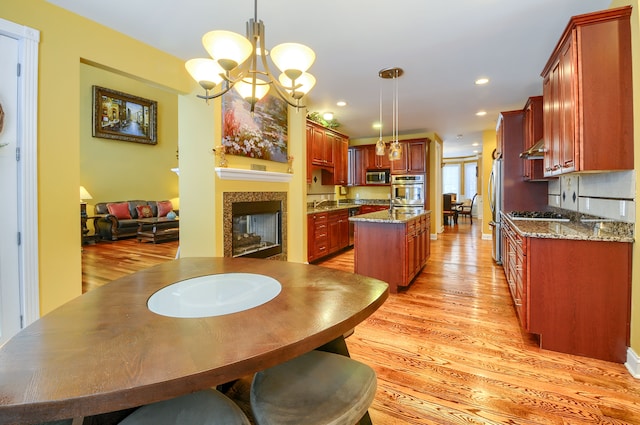 kitchen featuring stainless steel appliances, an island with sink, light stone counters, and hanging light fixtures